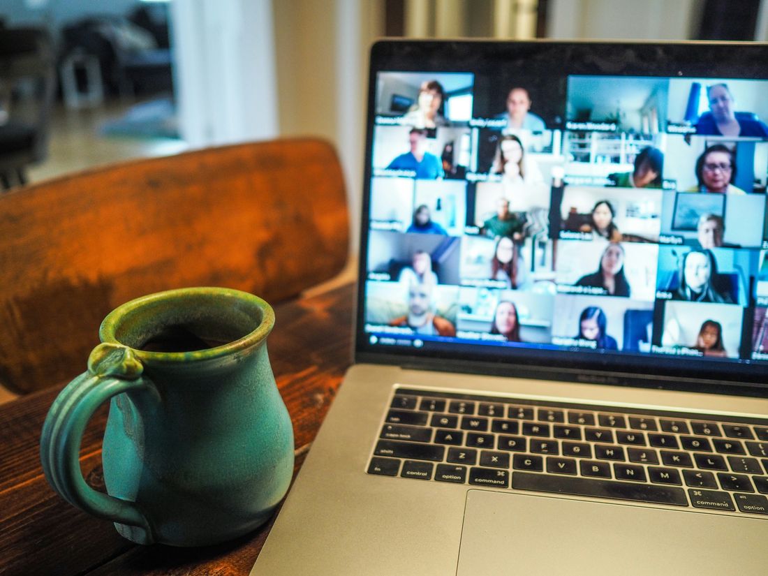 Laptop showing a video call with a distributed team, coffee mug beside it