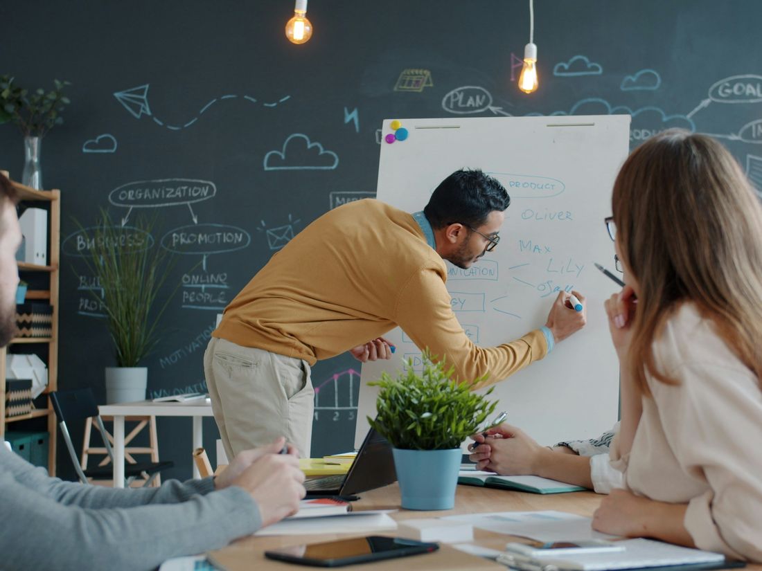 Consultant presenting strategy on a whiteboard to colleagues